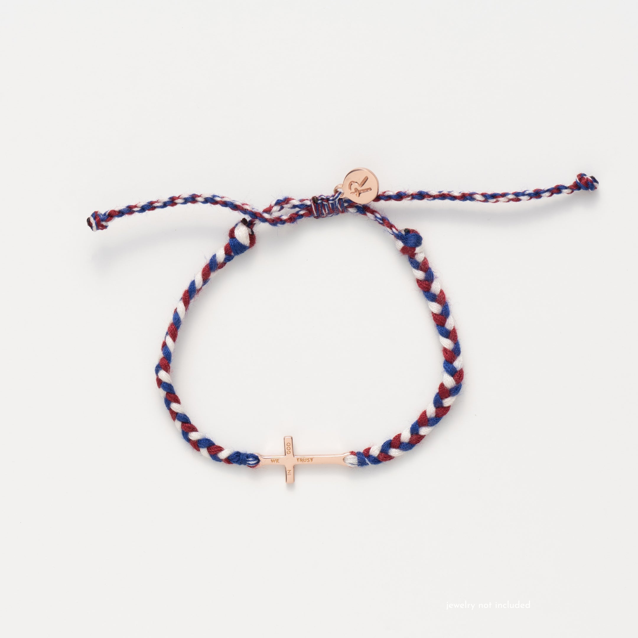 rose gold cross bracelet hand braided in red, white, blue cotton cord, engraved "WE TRUST IN GOD" with Rizen Jewelry and Made4Ministry round disc tag.