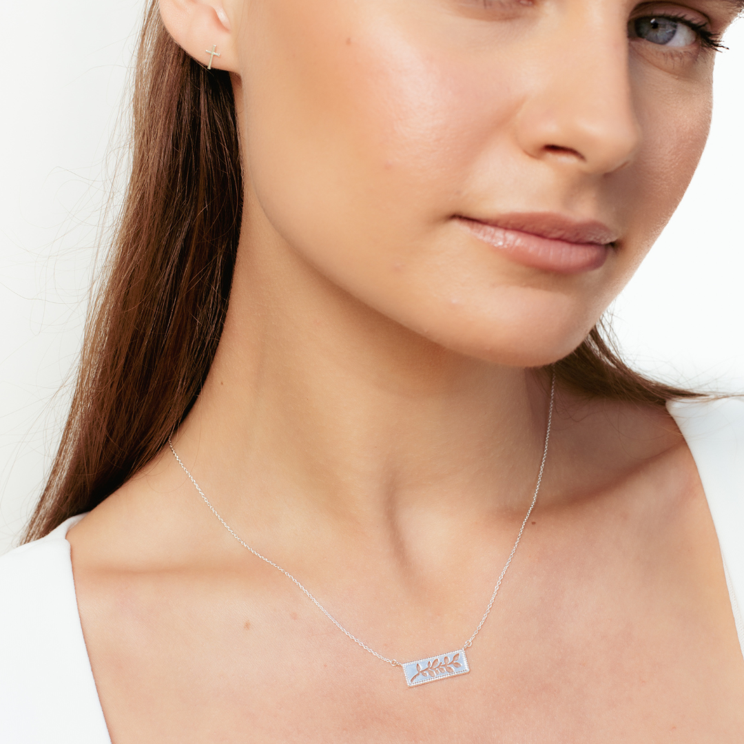 Close up of christian woman neck wearing sterling silver olive branch necklace and mini cross stud earrings from the Rooted collection by Rizen Jewelry. 