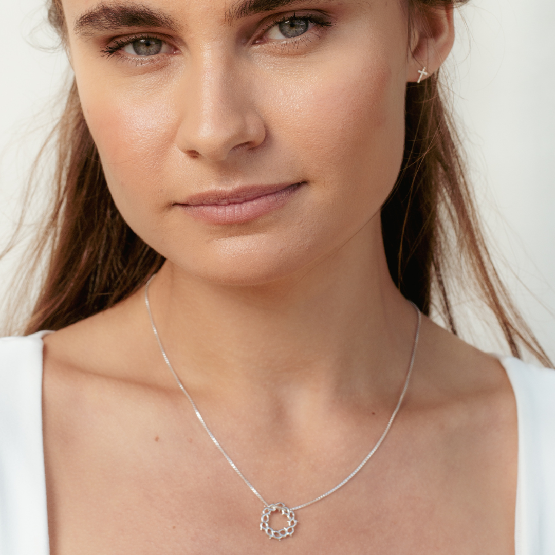 Close up of christian woman wearing sterling silver crown of thorns necklace and mini cross stud earrings from the Insignia Collection by Rizen Jewelry. 