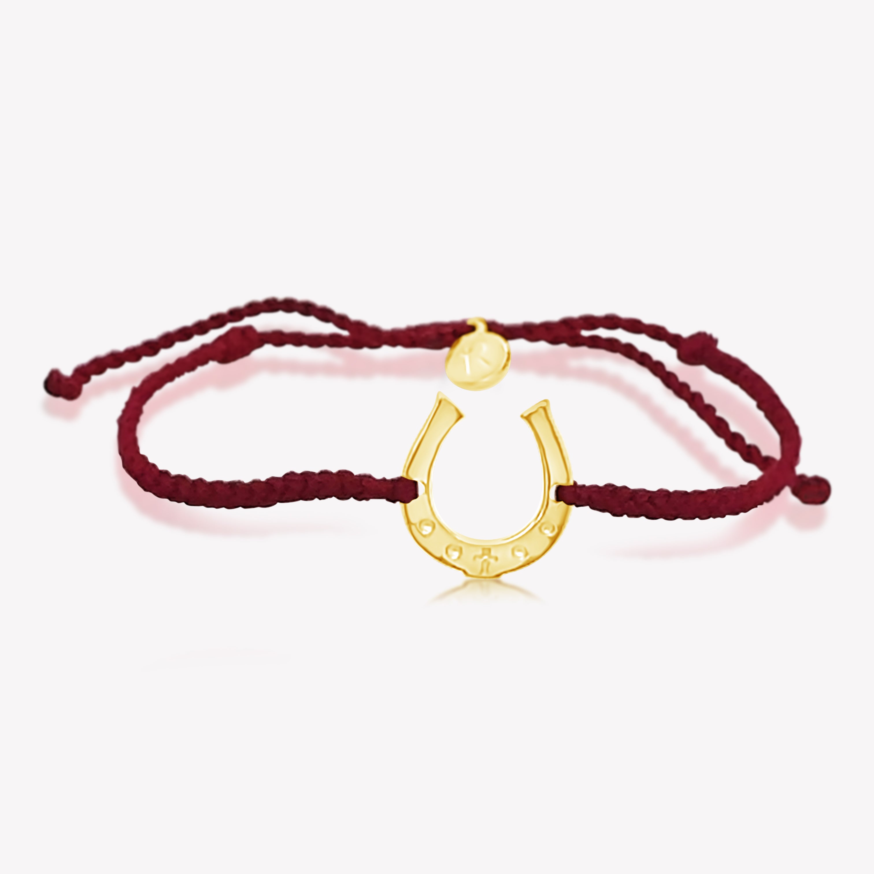 Close up of limited edition red cord friendship bracelet featuring a horseshoe pendant in gold from the Made4Ministry Collection by Rizen Jewelry benefitting Big Oak Ranch.