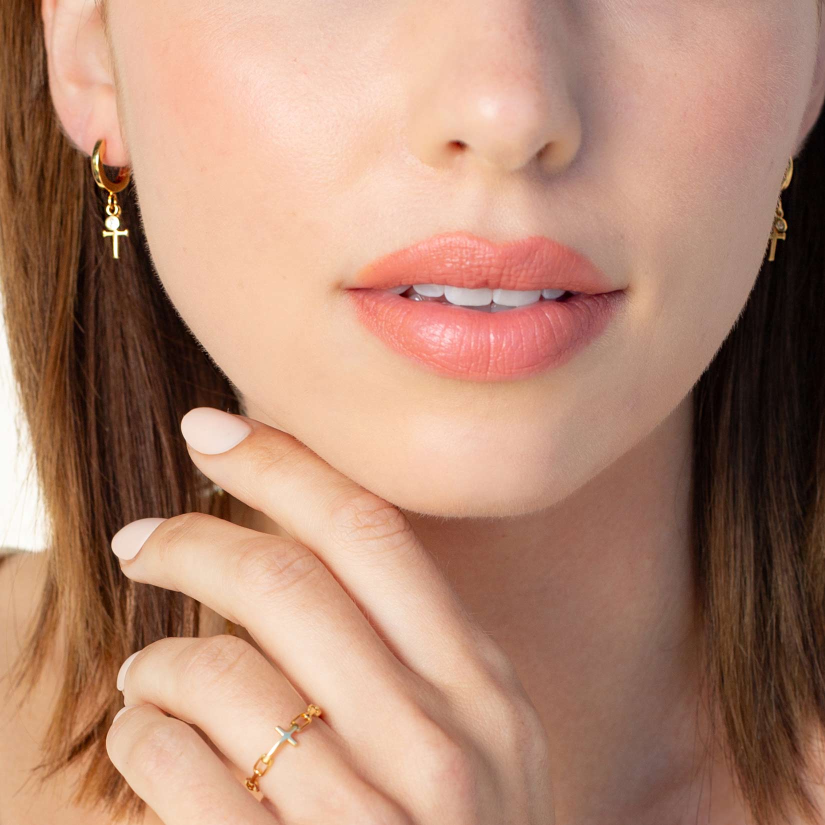 Close up of a christian woman wearing the 18k gold vermeil Cross Huggie Hoop Earring from the Calvary Collection by Rizen Jewelry.