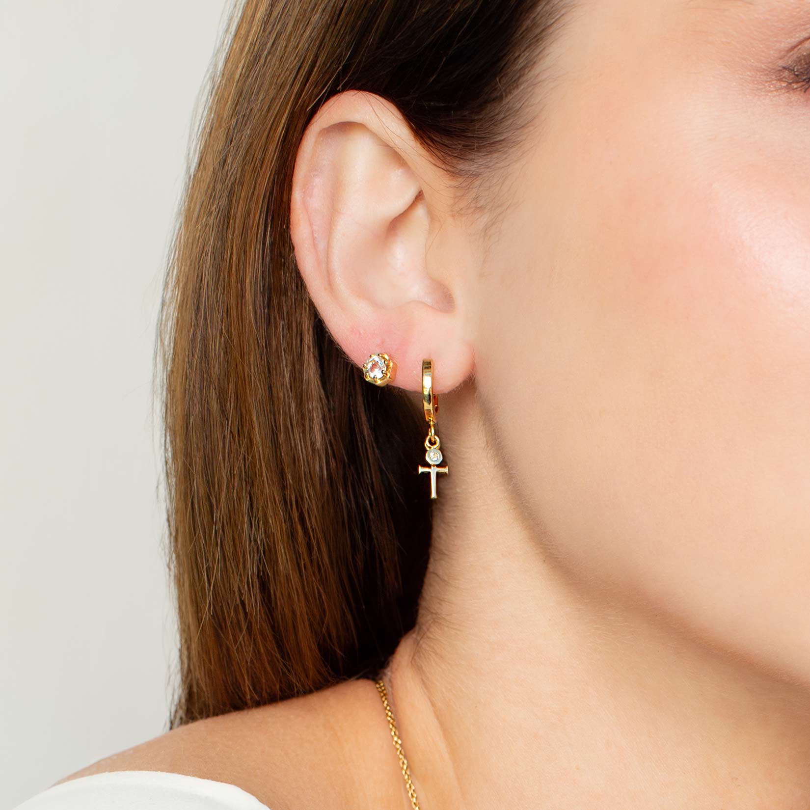 Close up of a christian woman wearing the 18k gold vermeil Cross Huggie Hoop Earring from the Calvary Collection by Rizen Jewelry.