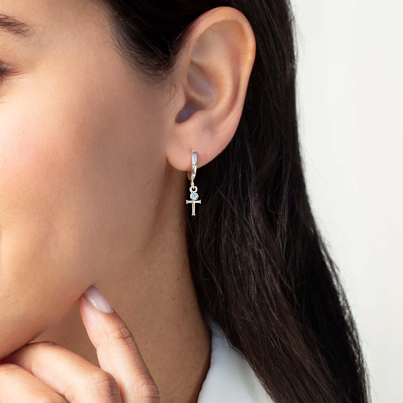 Close up of a christian woman wearing the sterling silver Cross Huggie Hoop Earring from the Calvary Collection by Rizen Jewelry.