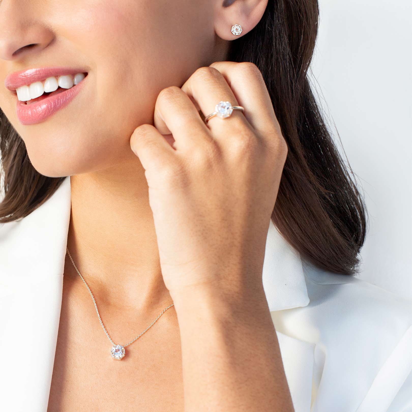 Close up of a christian woman wearing sterling silver white topaz Ebenezer Solitaire Earring, Ring and Necklace from the Chispa Collection by Rizen Jewelry.