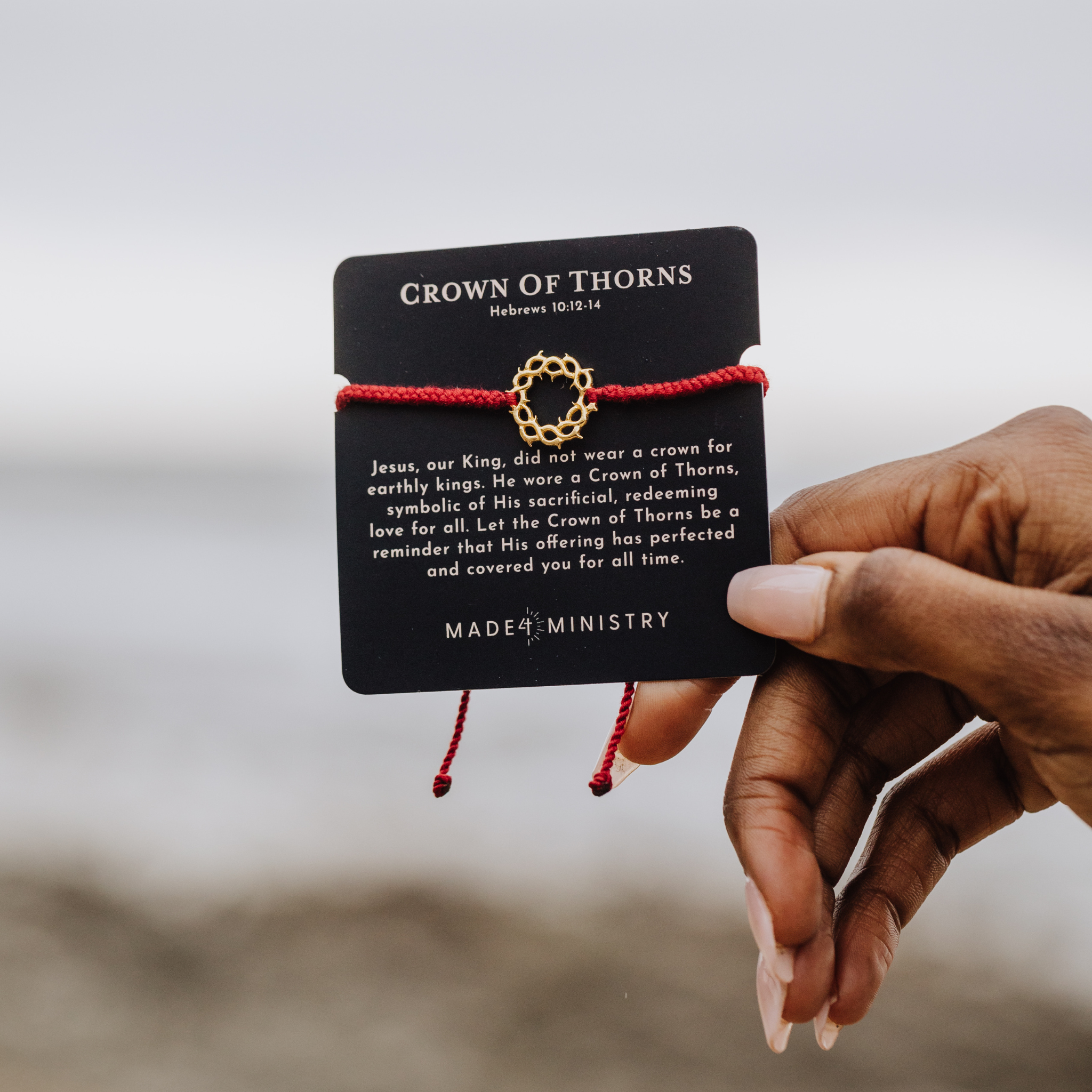 Rizen Jewelry christian model holding Made4Ministry Gold  Crown of Thorns Red Braided Cord Bracelet on scripture inspired devotion card.