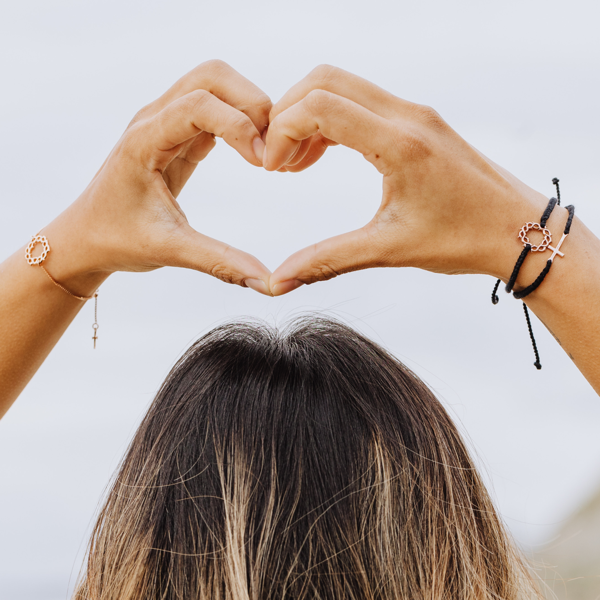 Rizen Jewelry model making heart sign with her hands wearing Black Rose Gold Child Of God Cross Bracelet layered with Cross of Thorns Adjustable  macrame friendship bracelet.