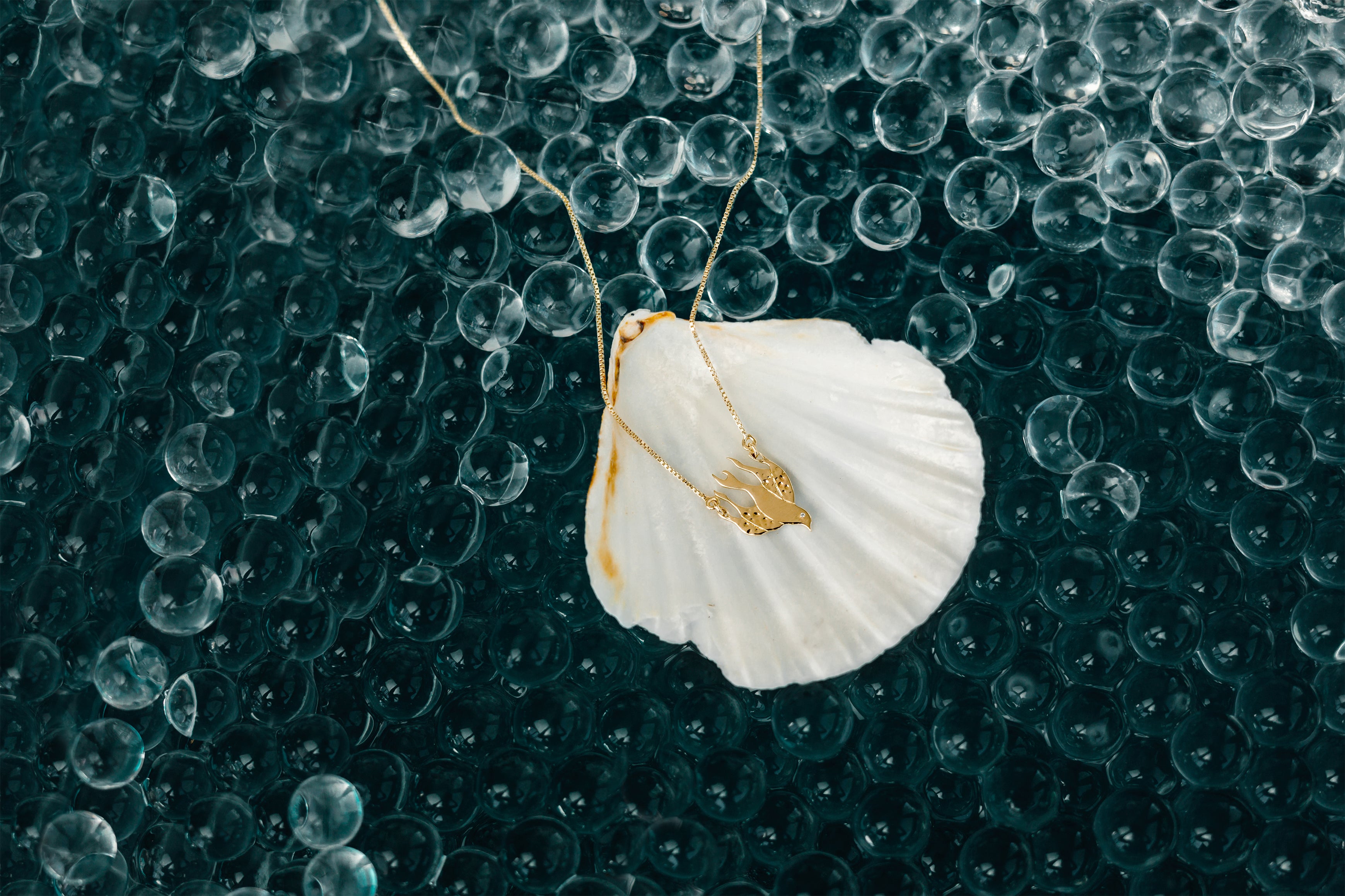 Rizen Jewelry 18kt yellow gold chispa de la dove necklace in scalloped shell on depth colored water marbles.
