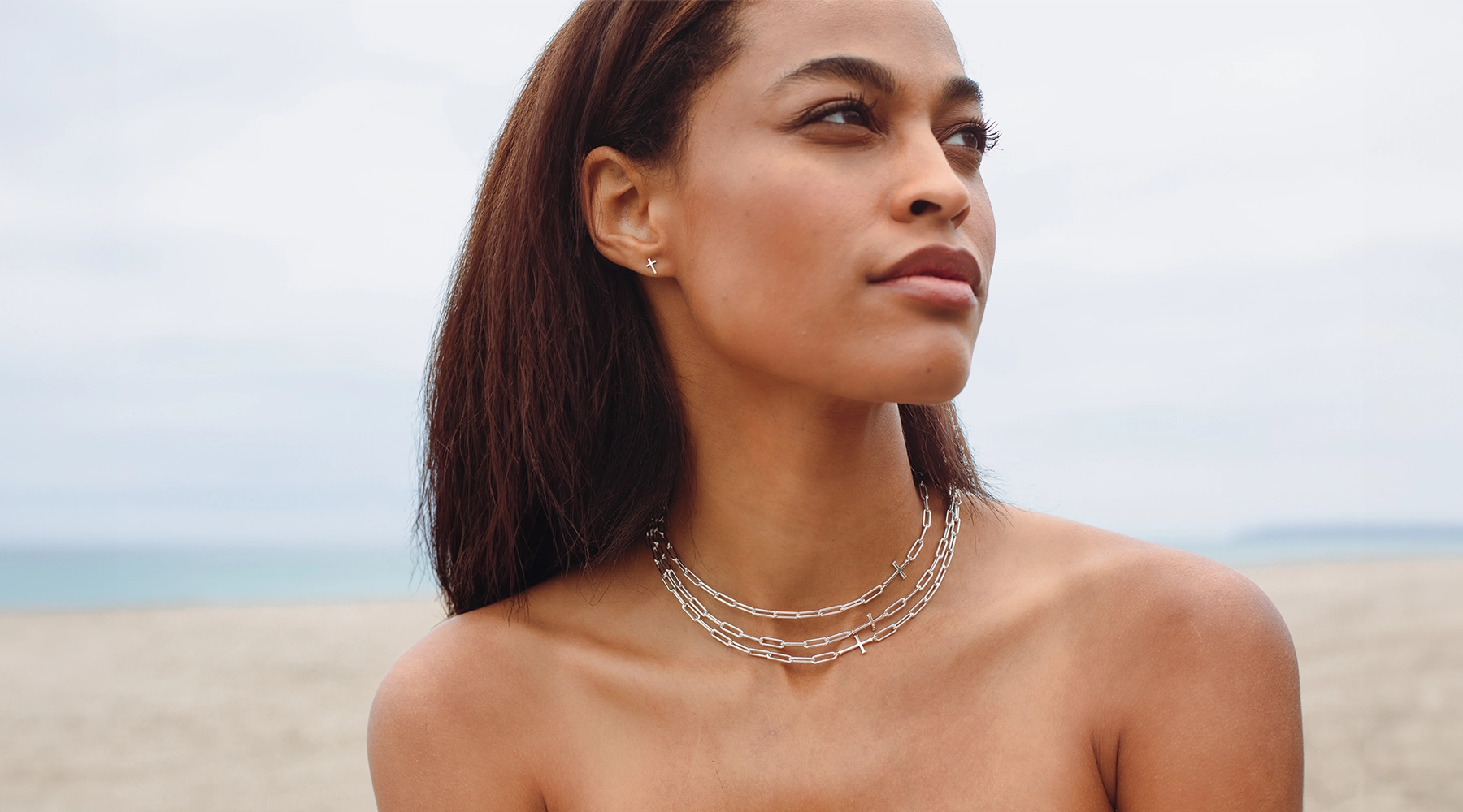 woman wearing three cross and paper link chain necklaces with mini cross stud earrings. 