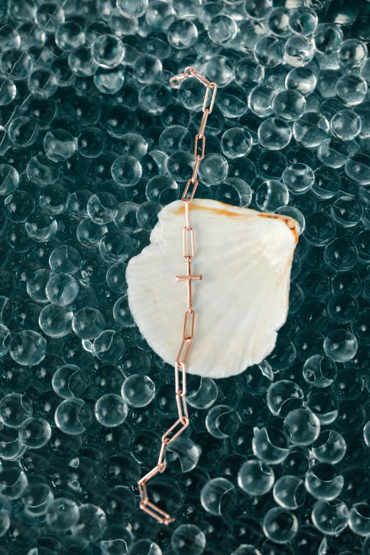 Rizen Jewelry 18kt rose gold vermeil chain breaker bracelet delicately balanced on called shell on reflective pool of depth colored marbles.