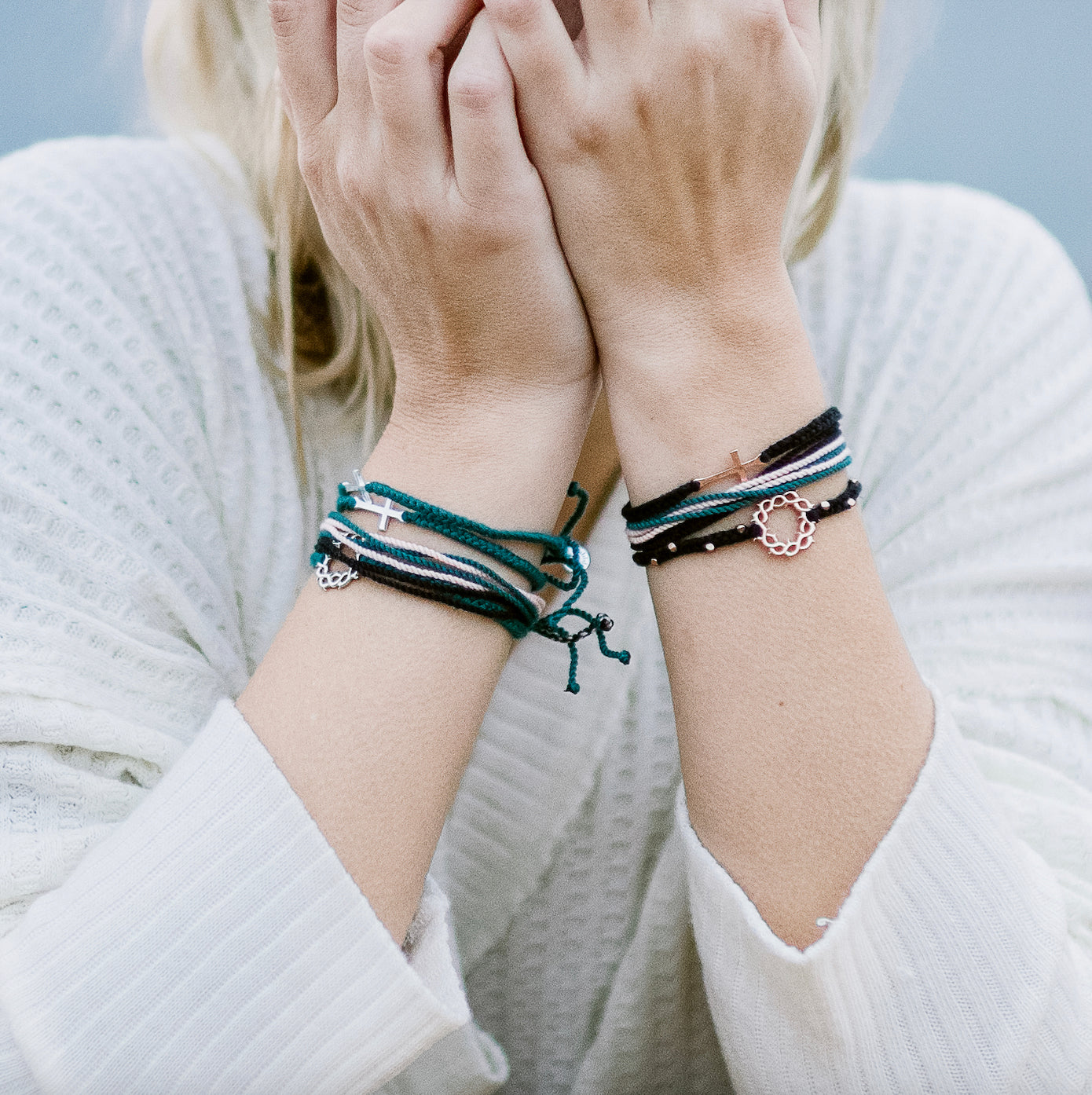 Christian model wearing the Black friendship bracelet with rose gold crown of thorns pendant and 8 dainty beads layered with rose gold azure blue, cross, and crown of thorns bracelets and multi cord black, azure blue, pink joyful Be Magnified bracelets.