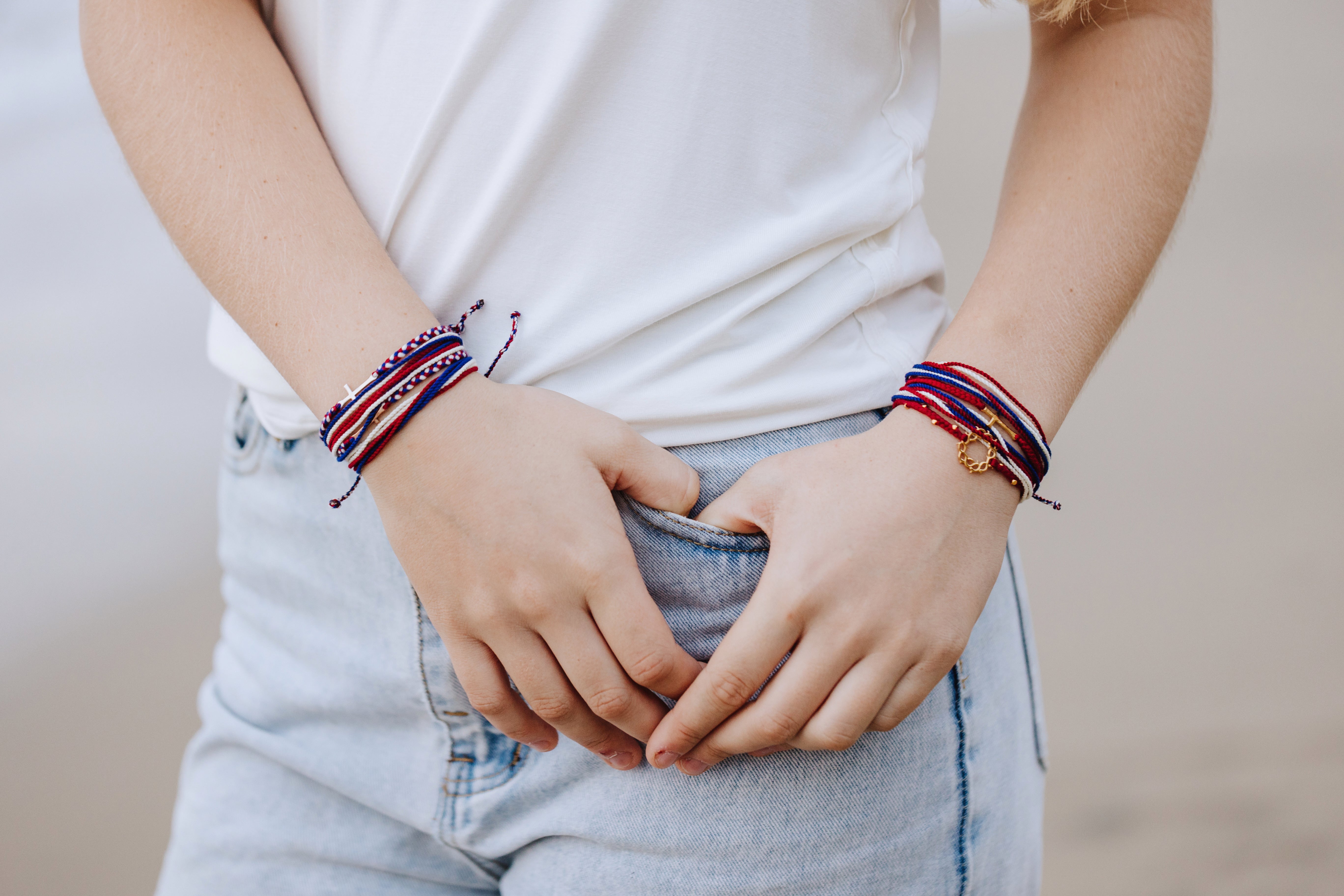 Christian Model wearing red white and blue be magnified peaceful bracelet layered with the multiple we trust in god cross bracelet, and garnet red crown of thorns and stay salty cross friendship bracelets by Rizen Jewelry Made 4 Ministries collection on both wrists.