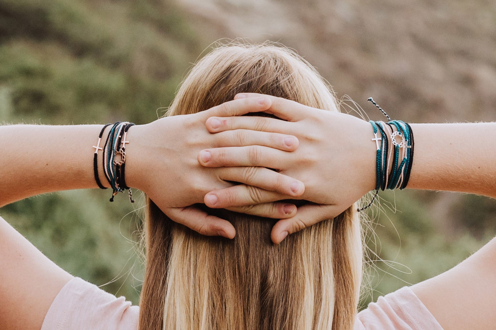 Christian model wearing the Black friendship bracelet with rose gold crown of thorns pendant and 8 dainty beads layered with rose gold azure blue, cross, and crown of thorns bracelets and multi cord black, azure blue, pink joyful Be Magnified bracelets. 