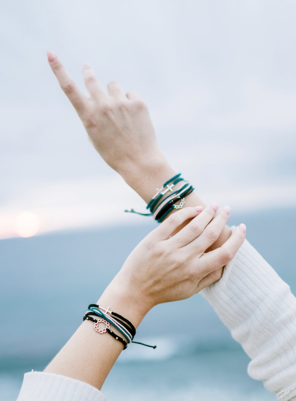 Christian model wearing silver cross bracelet engraved "STAY SALTY" hand braided azure blue cotton cords by Rizen Jewelry Made 4 Ministries collection. Layered with beaded crown of thorns and multi cord bracelets.