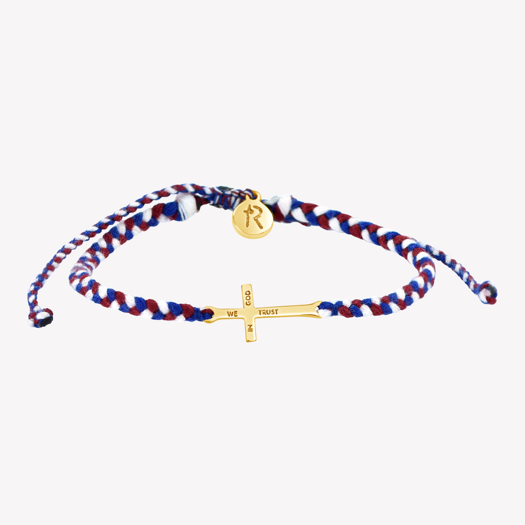 gold cross bracelet hand braided in red, white, blue cotton cord, engraved "WE TRUST IN GOD" with Rizen Jewelry and Made 4 Ministries round disc tag. 
