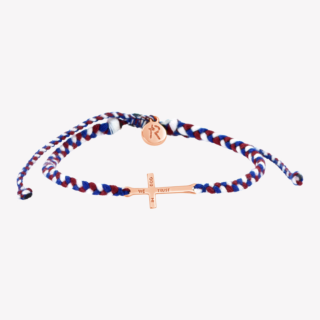 Rose gold cross bracelet hand braided in red, white, blue cotton cord, engraved "WE TRUST IN GOD" with Rizen Jewelry and Made 4 Ministries round disc tag.
