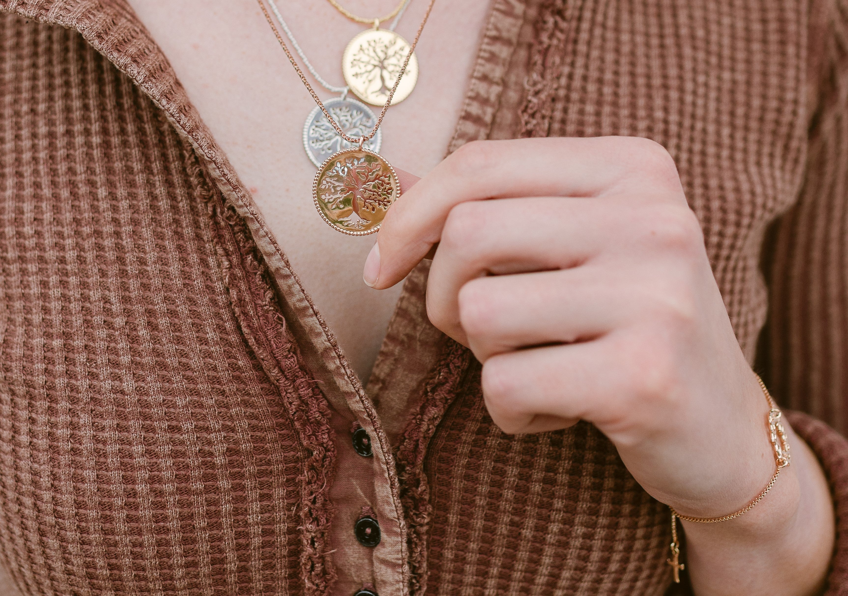 Christian model wearing 3 rooted olive tree necklaces in sterling silver, gold vermeil and holding rose gold vermeil pendant forward. 