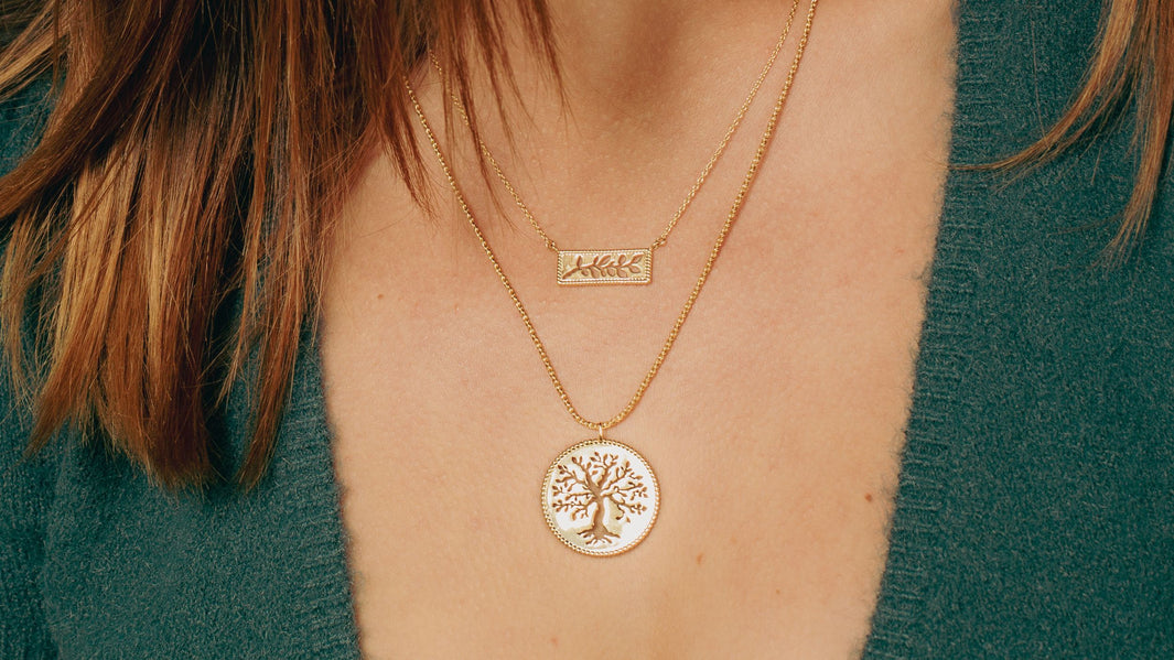 Christian model holding Rizen Jewelry Olive Tree Necklace in rose gold vermeil, layered with calvary cross necklace. 