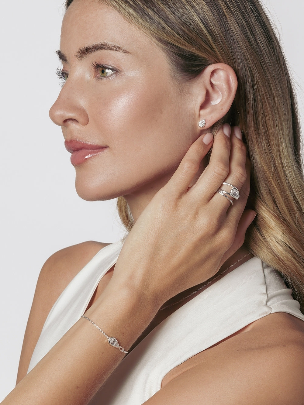 A christian female model is wearing the Rizen Jewelry Solace Teardrop Statemnet Ring crafted in sterling silver along with the matching bracelet and stud earring.