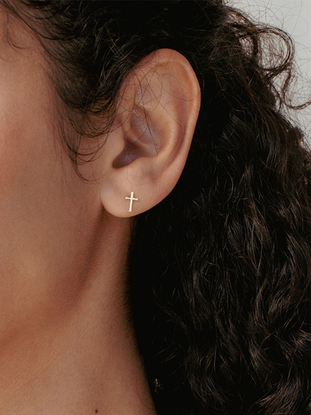 Women's Christian jewelry model is wearing Mini cross stud earrings in 18k gold plated from the Calvary collection. A timeless baptism gift by Rizen Jewelry.