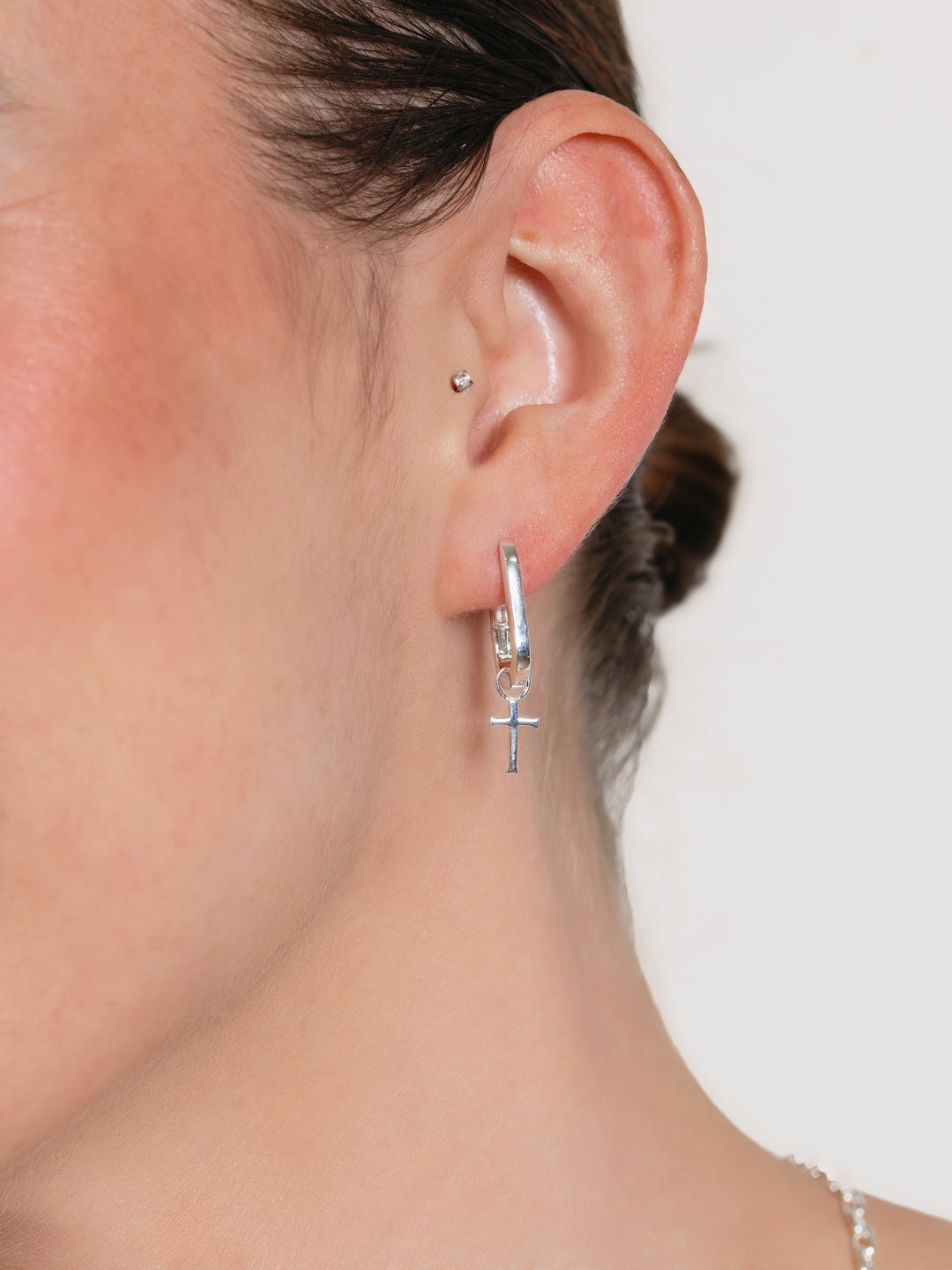 Close-up of a Christian woman's jewelry model wearing the Close-up of a Christian woman's jewelry model wearing the Sleek Sterling Silver Hoop Earrings with Cross Dangle by Rizen Jewelry. 