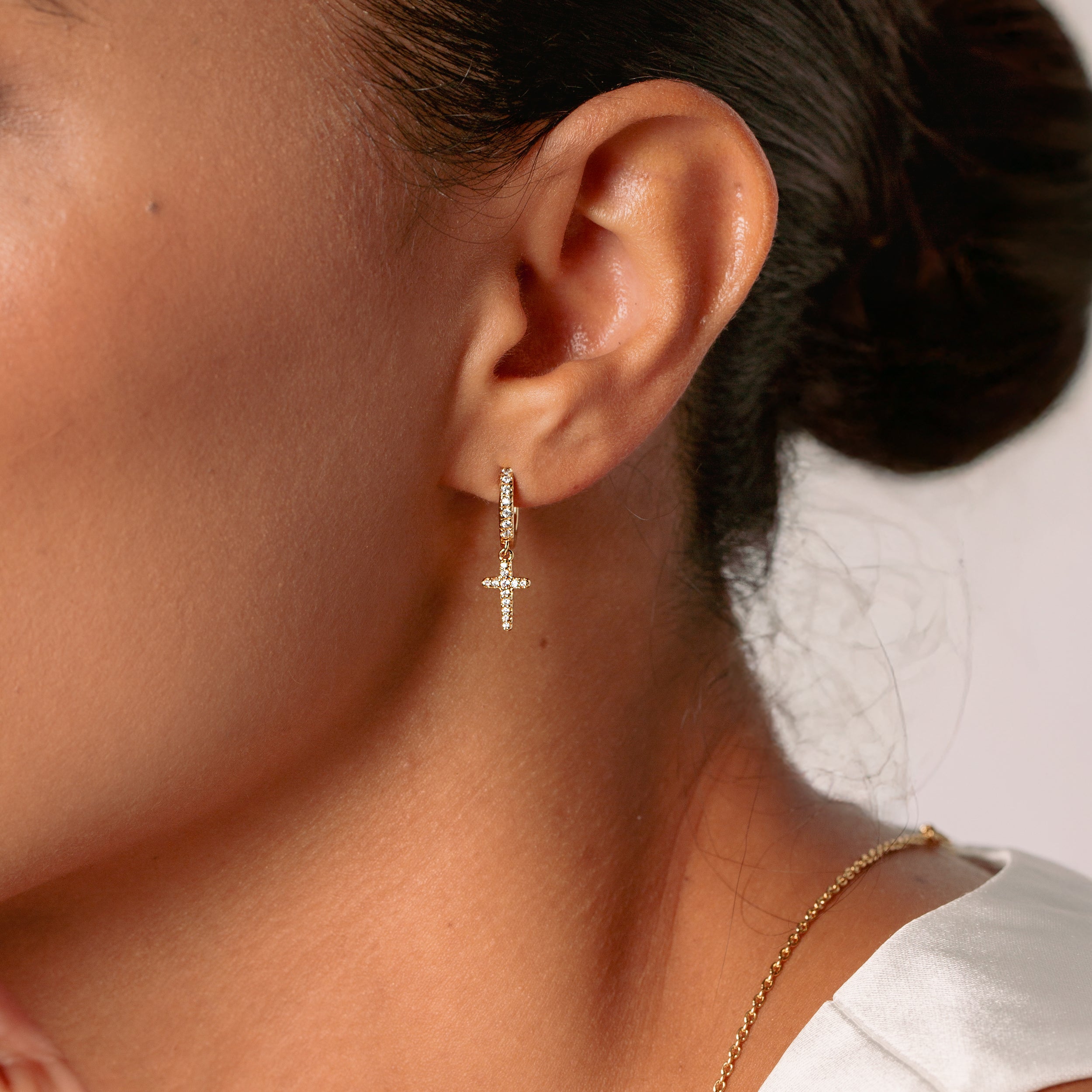 Close-up of a christian woman jewelry model wearing the Luminous Cross Pave Huggie Hoop Earring in 18k Gold Plated Sterling Silver from the Calvary Collection by Rizen Jewelry. 