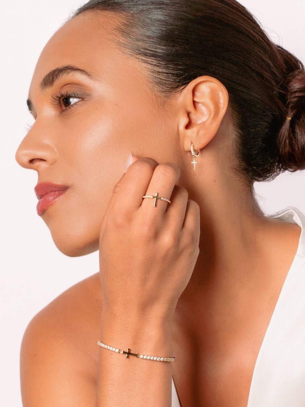 Women's Christian jewelry model is wearing the Luminous cross huggie hoop earrings in 18k gold plated alongside a bracelet and ring from the Calvary collection. A wonderful Christian Jewelry Gift by Rizen Jewelry.