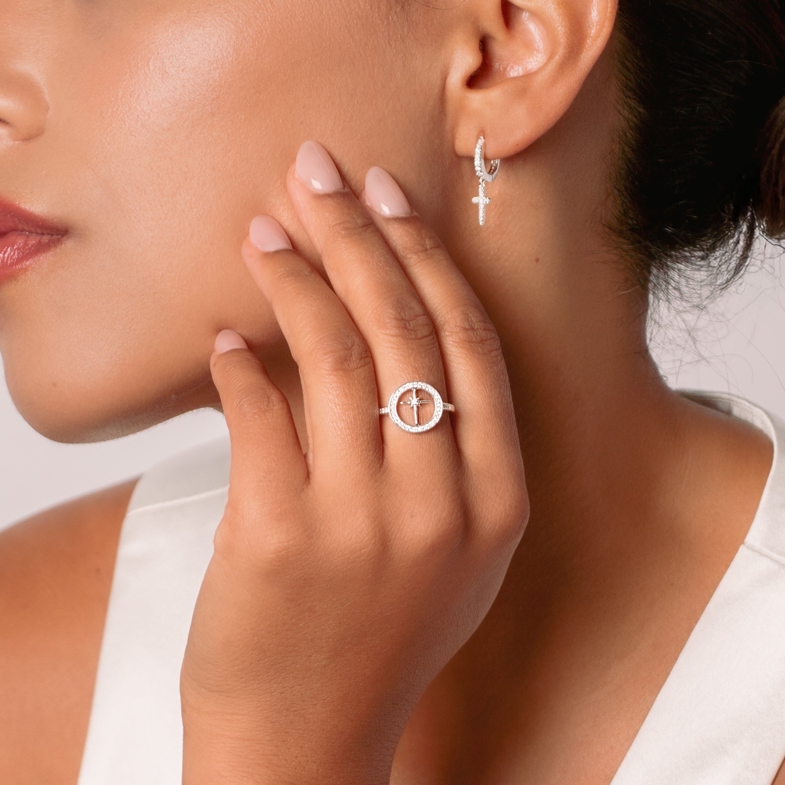 Close-up of a christian woman jewelry model wearing the luminous cross pave earrings and adoring star compass ring all designed by Rizen Jewelry. 