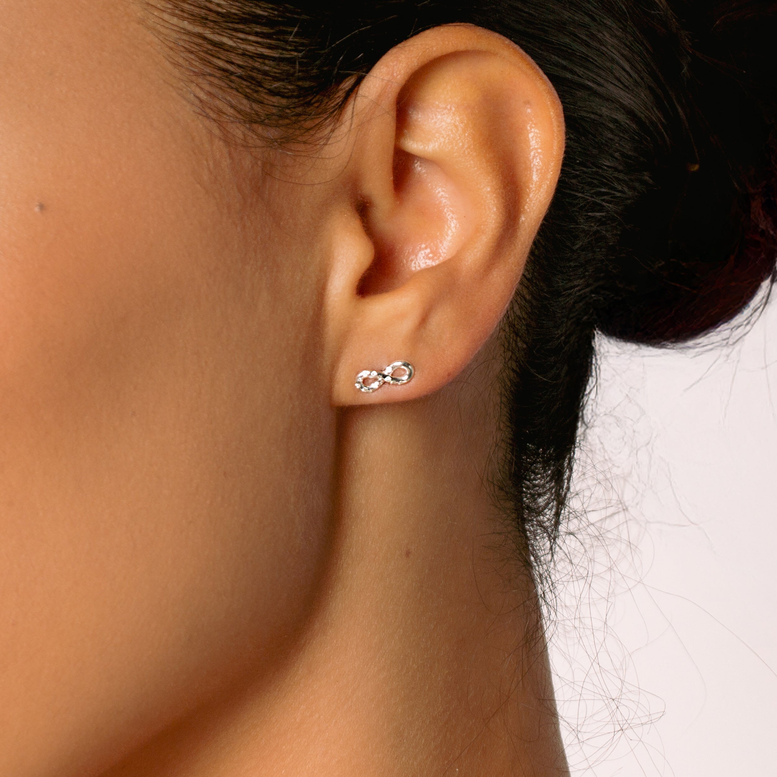 Close-up of a christian woman jewelry model  wearing the sterling silver infinity stud earrings from the Infinite Grace Collection by Rizen Jewelry. 