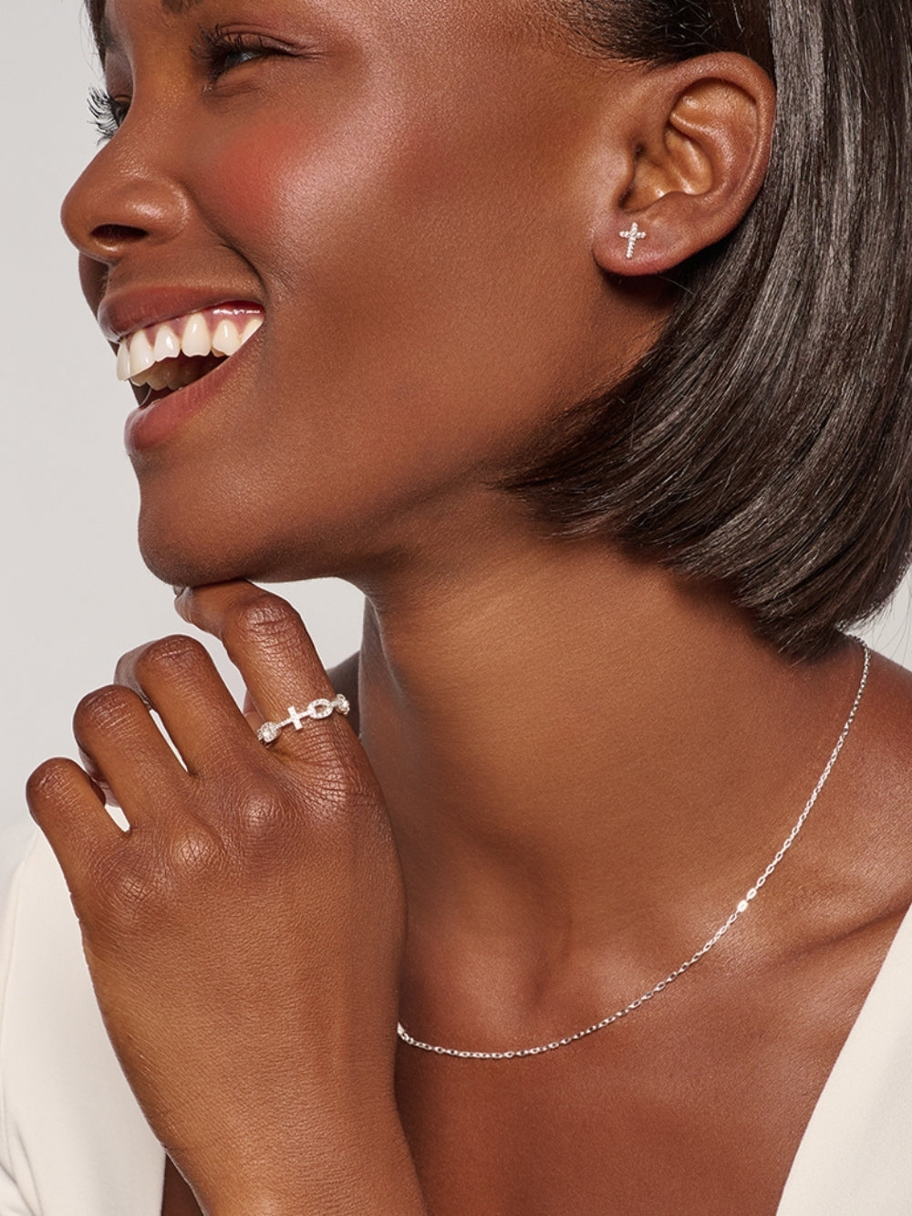 Female christian jewelry model wearing the Luminous Cross Pavé Stud Earrings, delicate silver cross studs that shine with faith, with the matching necklace and ring designed by Rizen Jewelry. 