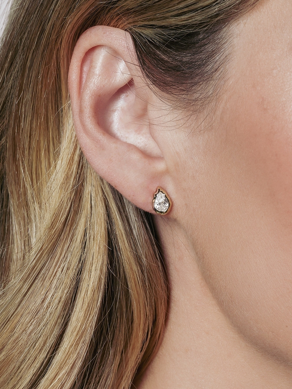 A close-up of a Christian woman's ear featuring the Rizen Jewelry Solace Teardrop Stud Earring in a 18k gold finish. 