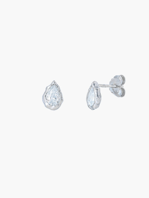 A pair of Rizen Jewelry Solace Tear Stud Earrings  in sterling silver stud.  They feature a tear drop shaped simulated diamond shown on a plain light gray background.