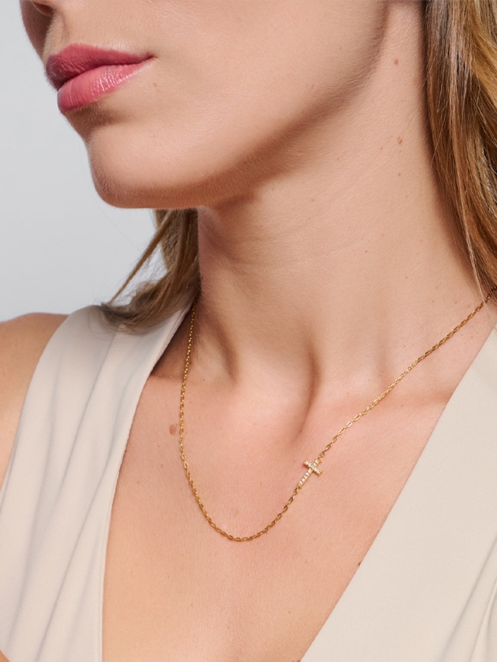 Female model wearing the Delicate Cross Chain Breaker Necklace, an 18k gold-plated pavé cross pendant resting at the collarbone.