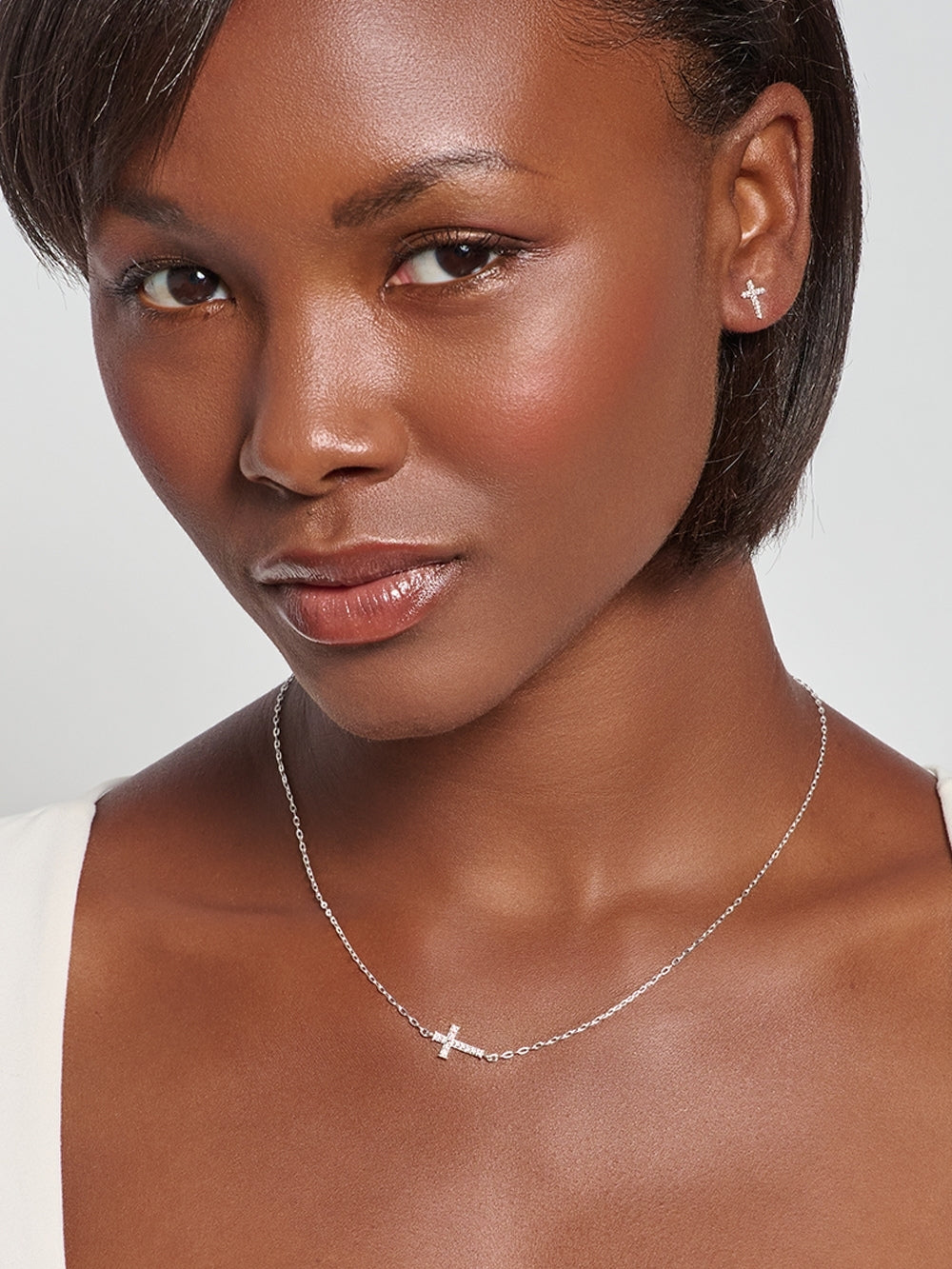 Female model wearing the Delicate Cross Chain Breaker Necklace, a sterling silver pavé cross pendant resting at the collarbone.