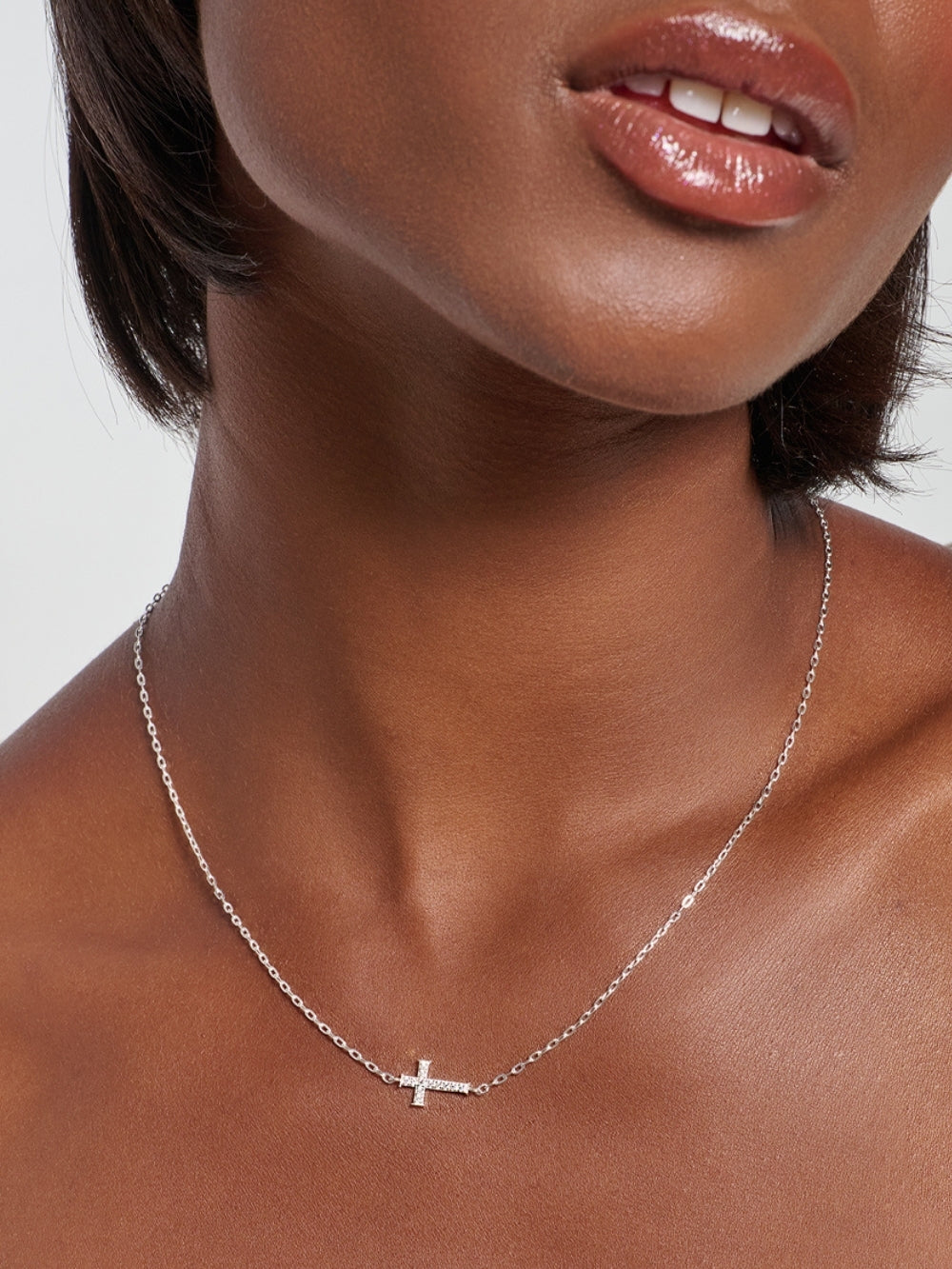 Female model wearing the Delicate Cross Chain Breaker Necklace, a sterling silver pavé cross pendant resting at the collarbone.