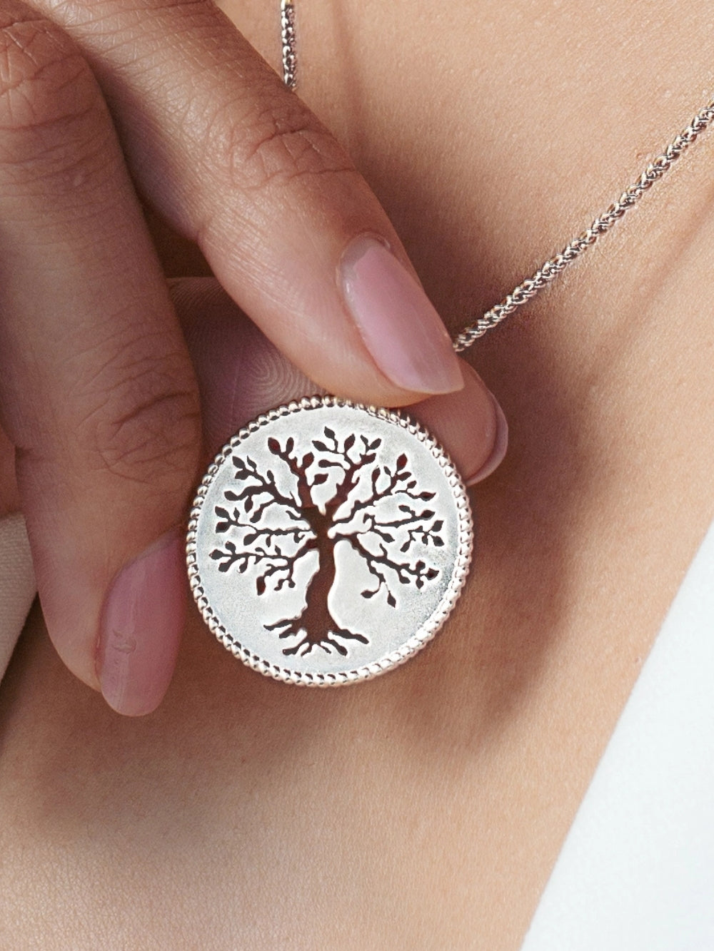 Close up of Christian woman holding and wearing the Olive Tree Necklace in sterling silver from the Rooted Collection by Rizen Jewelry.