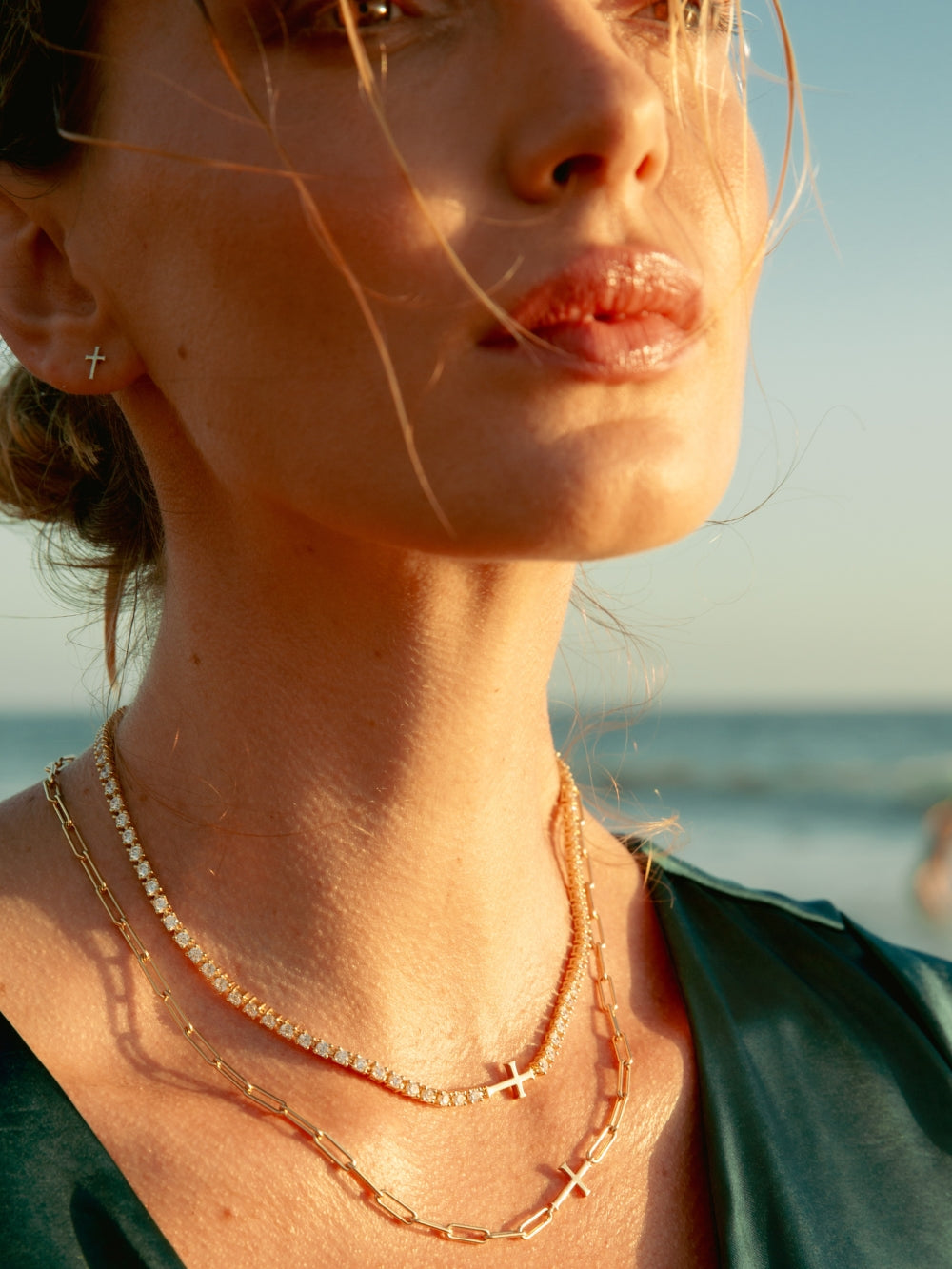 Women's Christian jewelry model wearing the Luminous cross tennis necklace in 18k gold plated along side the chain breaker cross necklace from the Calvary collection by Rizen Jewelry.