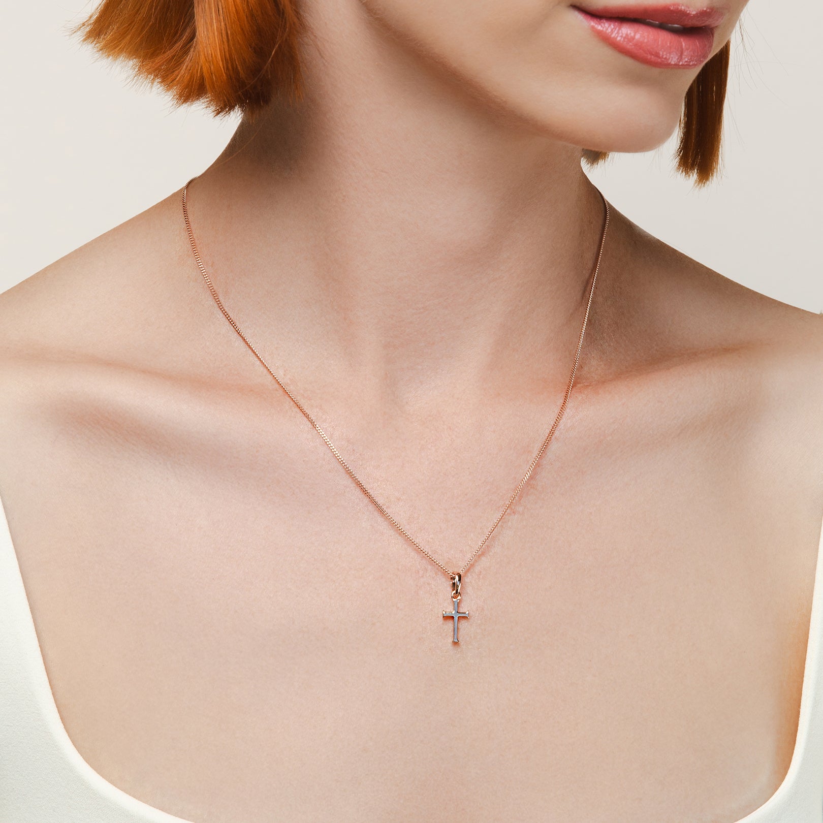 A Christian model wearing the small cross pendant in 18k rose gold vermeil from the Calvary collection by Rizen Jewelry.