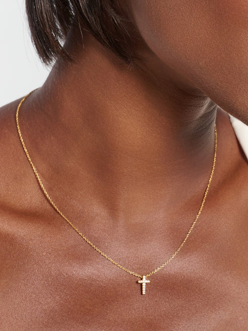 8.	Female model wearing the Dainty Luminous Cross Pavé Pendant Necklace, a radiant gold cross pendant resting at the collarbone by Rizen Jewelry