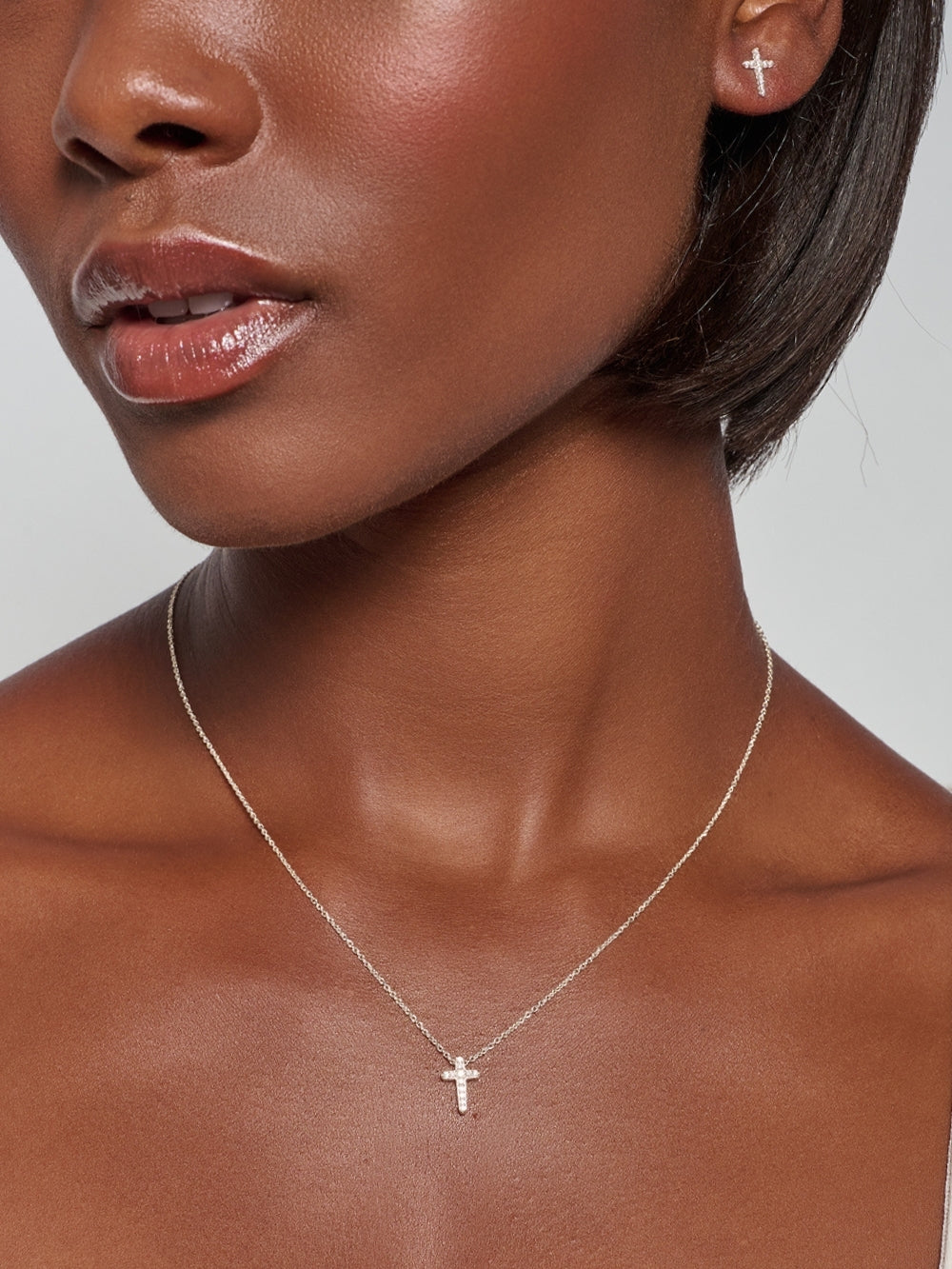 Female model wearing the Dainty Luminous Cross Pavé Pendant Necklace, a radiant silver cross pendant resting at the collarbone, with the matching cross earrings by Rizen Jewelry.