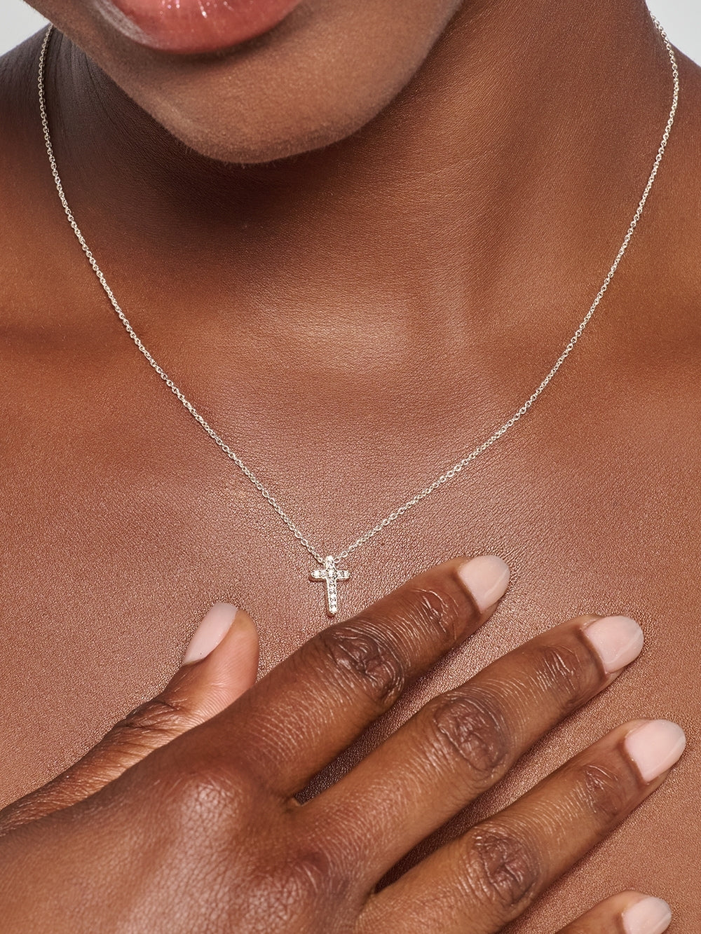 A close-up of a female model wearing the Dainty Luminous Cross Pavé Pendant Necklace, a radiant silver cross pendant resting at the collarbone