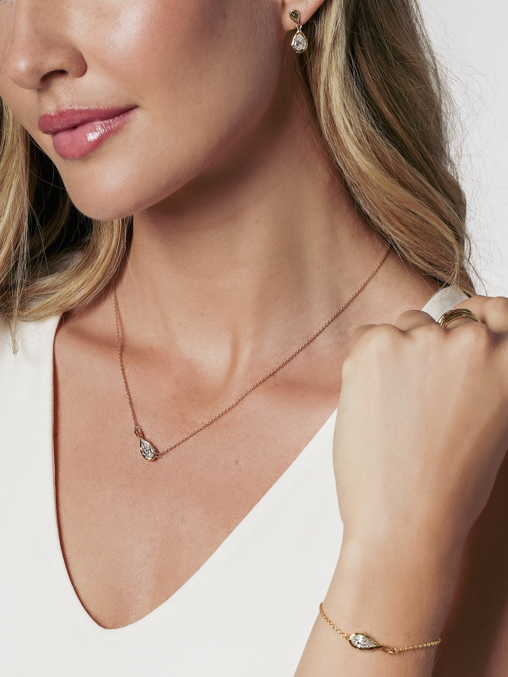 A close-up lifestyle shot of a christian woman from Rizen Jewerly wearing a delicate gold solace tear necklace with a teardrop infinity pendant and a matching gold bracelet, drop earrings and ring.
