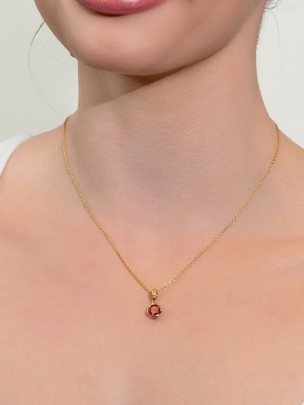 Women's Christian jewelry model wears the Ruby Fully Known Prayer Pendant by Rizen Jewelry features a round brilliant-cut light lab ruby stone is cradled in 18k gold plating over sterling silver setting. The pendant symbolizes passion, redemption, value, and the month of July.