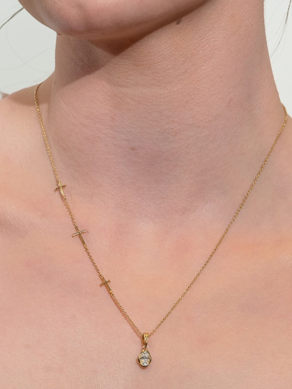 Women's Christian jewelry model wears the Calvary Cross necklace styled with the White Sapphire Fully Known Prayer Pendant by Rizen Jewelry features A radiant oval brilliant-cut white sapphire pendant, reflecting innocence, our new identity, and the luminous pure heart of April, cradled gently in refined 18k gold plating over sterling silver. 