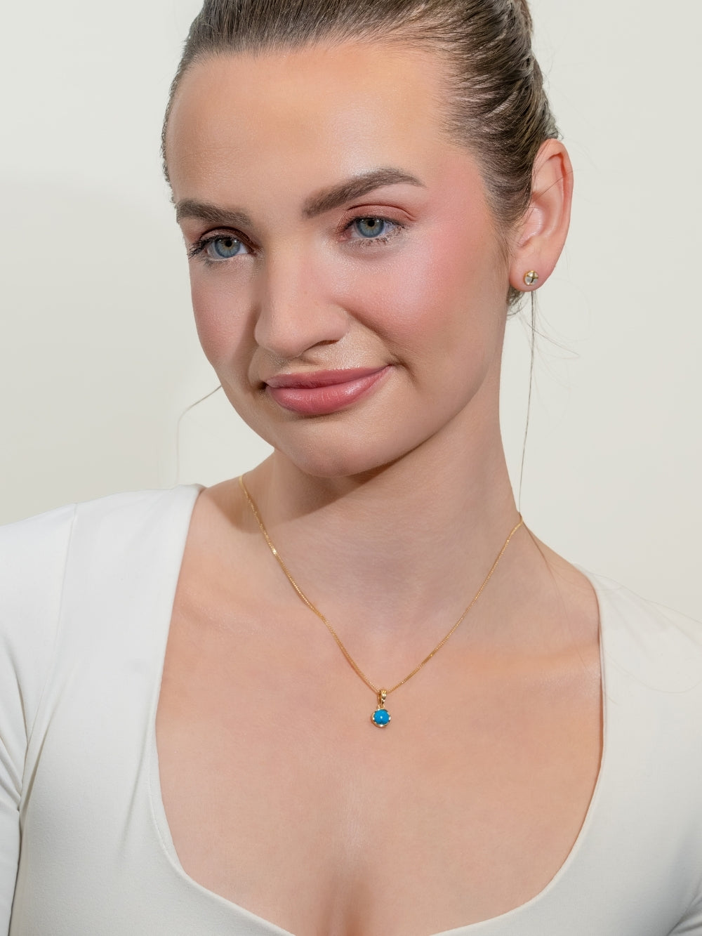 Woman's Christian jewelry model wearing the Turquoise Fully Known Prayer Pendant by Rizen Jewelry features a round cabochon turquoise stone is cradled in 18k gold plating over sterling silver setting. The pendant symbolizes Restoration, Leadership, Favor, and the month of December.