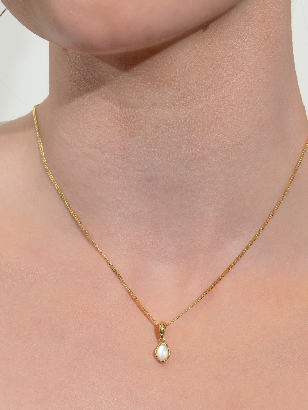 Woman's Christian jewelry model wears a White Mother of Pearl Fully Known Prayer Pendant by Rizen Jewelry features an  oval cabochon Mother of Pearl stone  cradled in 18k gold plating over sterling silver. The pendant symbolizes Transformation, Sacred, Beauty, and the month of June.