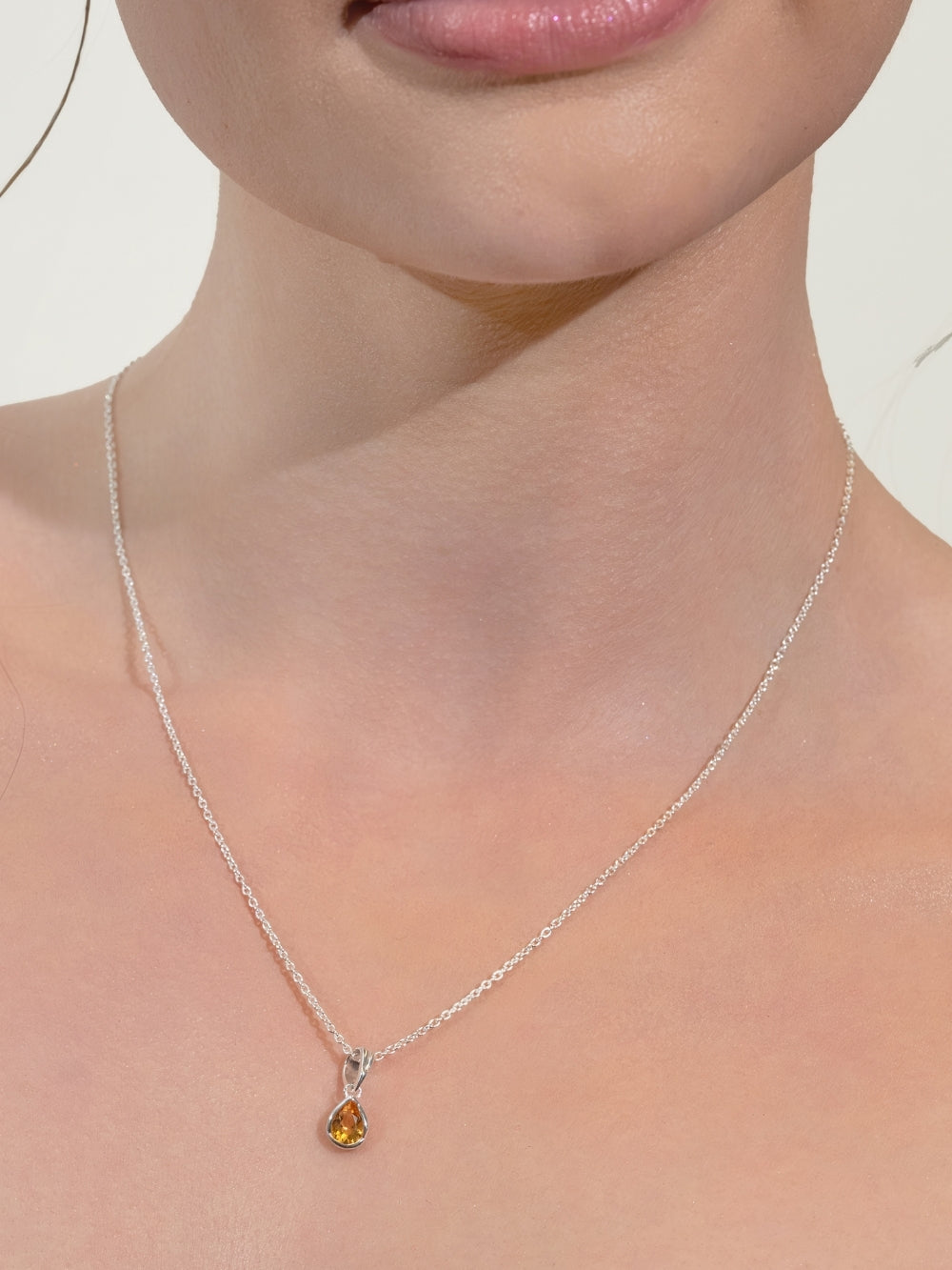 A pear-cut light citrine stone is cradled in a sterling silver setting. The pendant symbolizes wisdom, truth, guidance, and the month of November and is worn by a women's Christian jewelry model on a silver cable chain 
