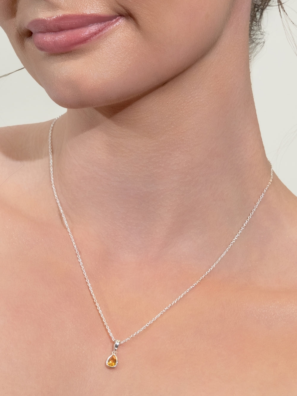 A pear-cut light citrine stone is cradled in a sterling silver setting. The pendant symbolizes wisdom, truth, guidance, and the month of November and is worn by a women's Christian jewelry model on a silver cable chain 