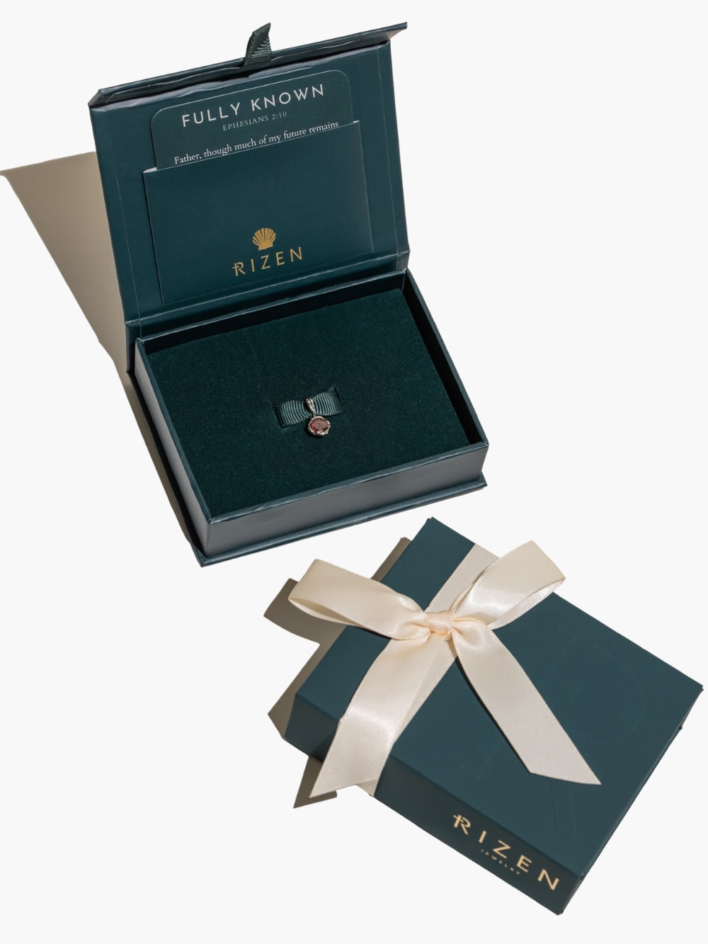 The Ruby Fully Known Prayer Pendant by Rizen Jewelry features a  round brilliant-cut light lab ruby stone cradled in a sterling silver setting. The pendant symbolizes passion, redemption, value, and the month of July is ready to gift in beautiful packaging. 