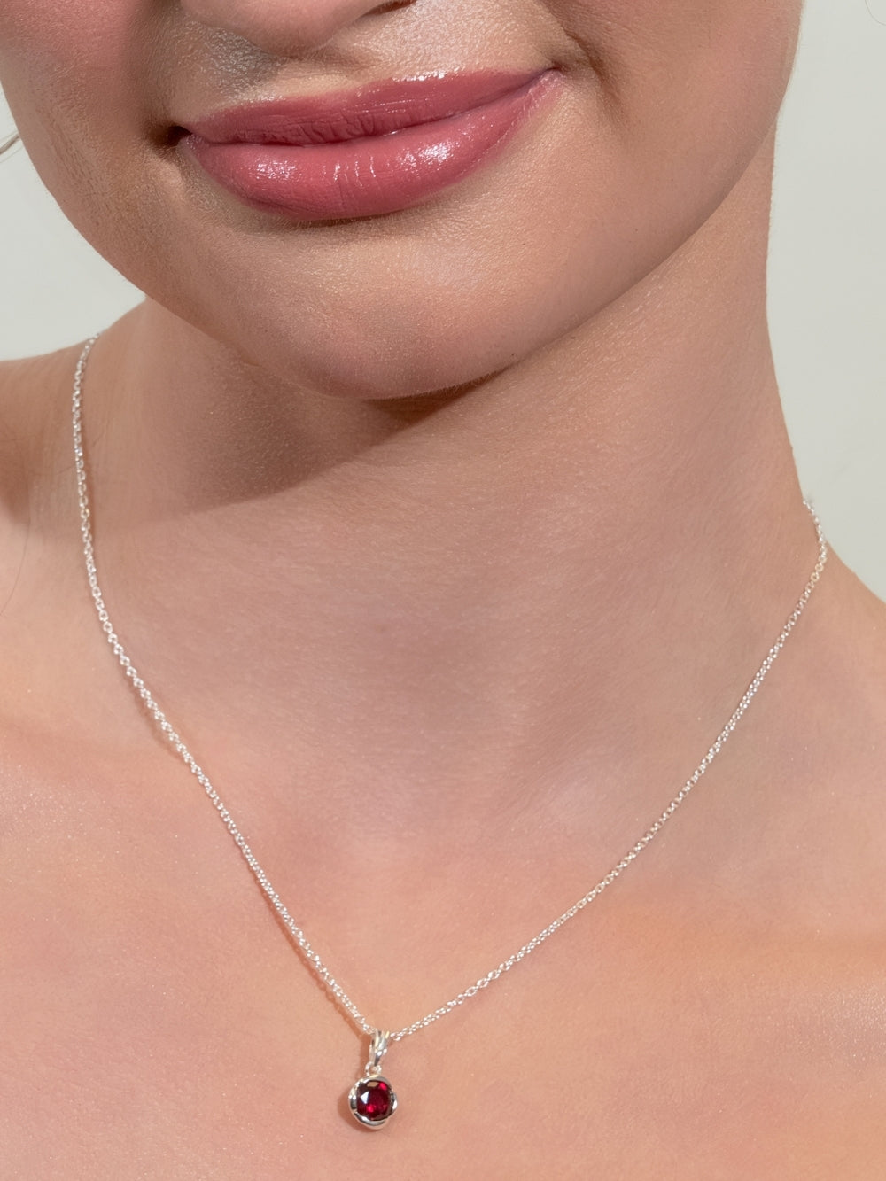 Women's Christian jewelry model wears The Ruby Fully Known Prayer Pendant by Rizen Jewelry features a  round brilliant-cut light lab ruby stone cradled in a sterling silver setting. The pendant symbolizes passion, redemption, value, and the month of July.