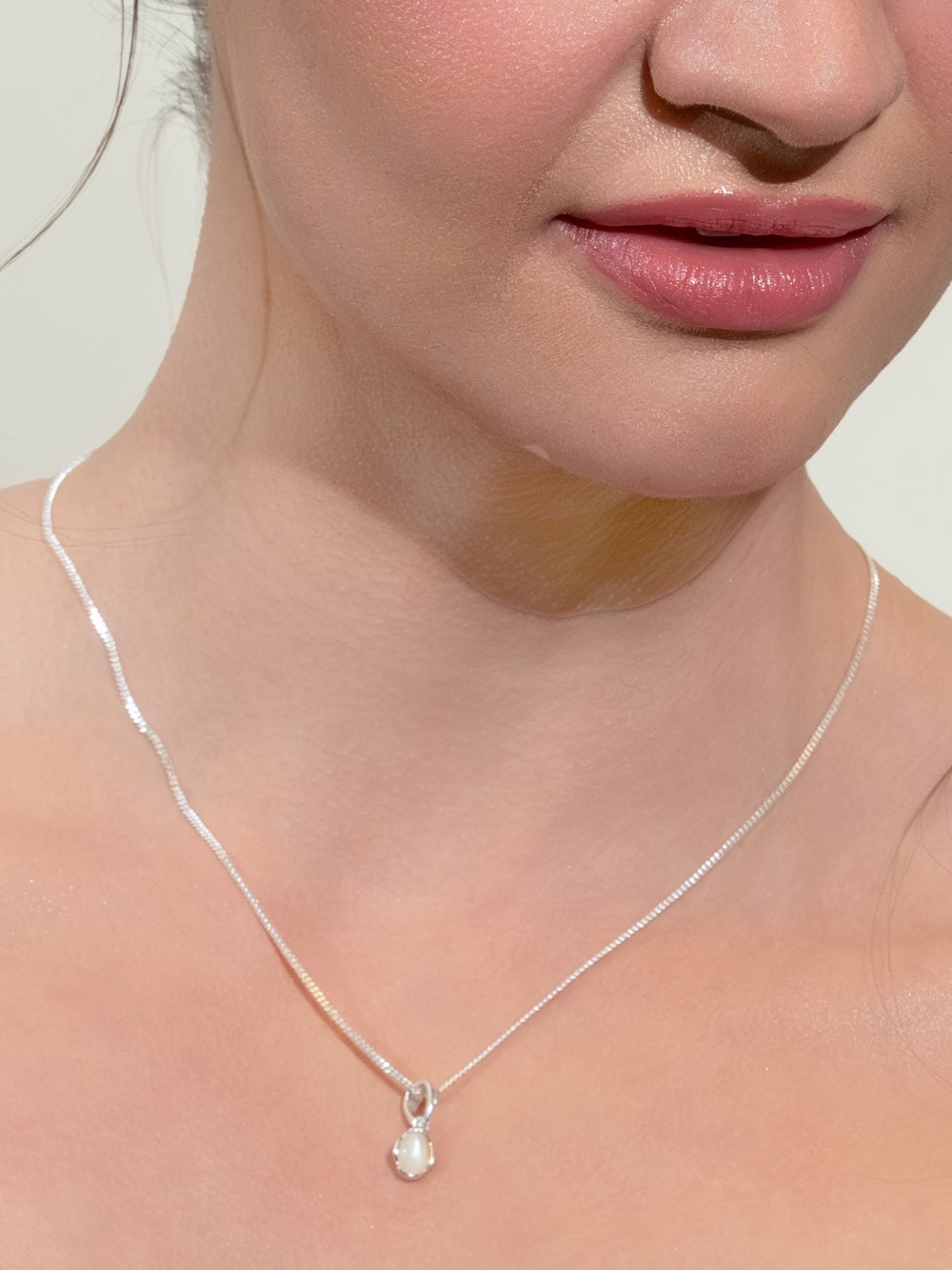 Woman's Christian jewelry model wears the White Mother of Pearl Fully Known Prayer Pendant by Rizen Jewelry features an oval cabochon Mother of Pearl stone  cradled in sterling silver setting. The pendant symbolizes Transformation, Sacred, Beauty, and the month of June.